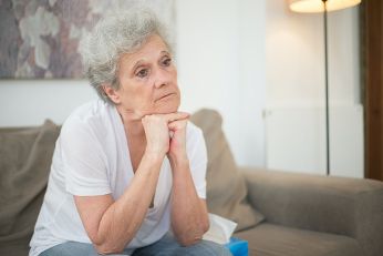 ältere Frau sitzt alleine auf einer Couch