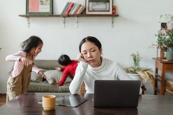 Frau sitzt am Laptop mit Kindern im Hintergrund