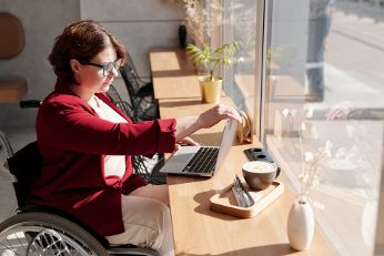 Frau im ROllstuhl sitzt mit Laptop vor dem Fenster