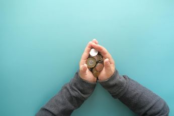 Das Bild zeigt eine Hand vor einem türkisen Hintergrund. Die Hände sind zu einer Mulde gefaltet und darin befinden Sich Euromünzen.