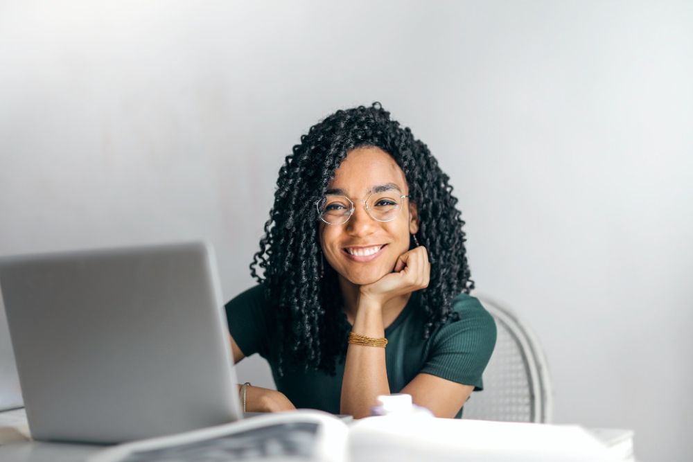 Lächelnde Frau sitzt am Tisch vor Laptop 