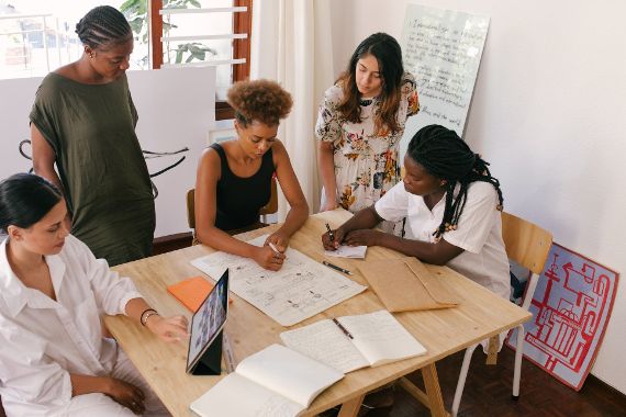 Fünf Frauen stehen um einen Tisch und arbeiten an einem Projekt