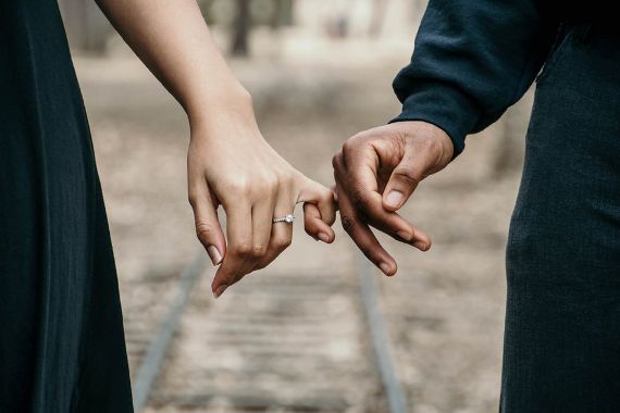 Mann in Schwarz und Frau im schwarzen Kleid halten sich gegenseitig am kleinen Finger